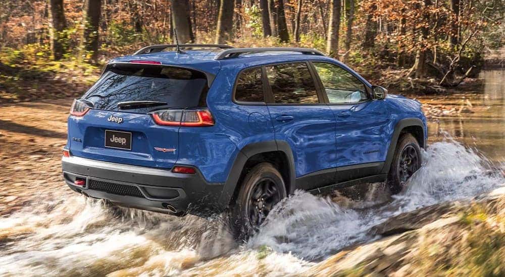 A blue 2021 Jeep Cherokee is shown from the rear off-roading through water.