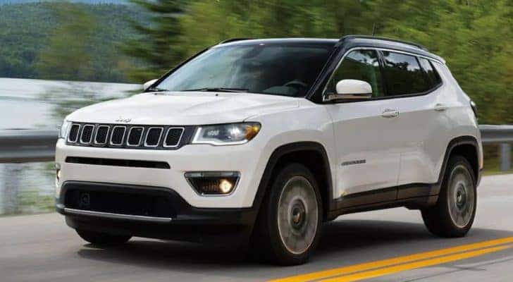 A white 2021 Jeep Compass is driving past a pond for the Jeep Compass Buyers Guide.