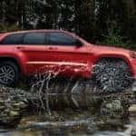 A red 2021 Jeep Grand Cherokee Trailhawk is driving through a puddle.