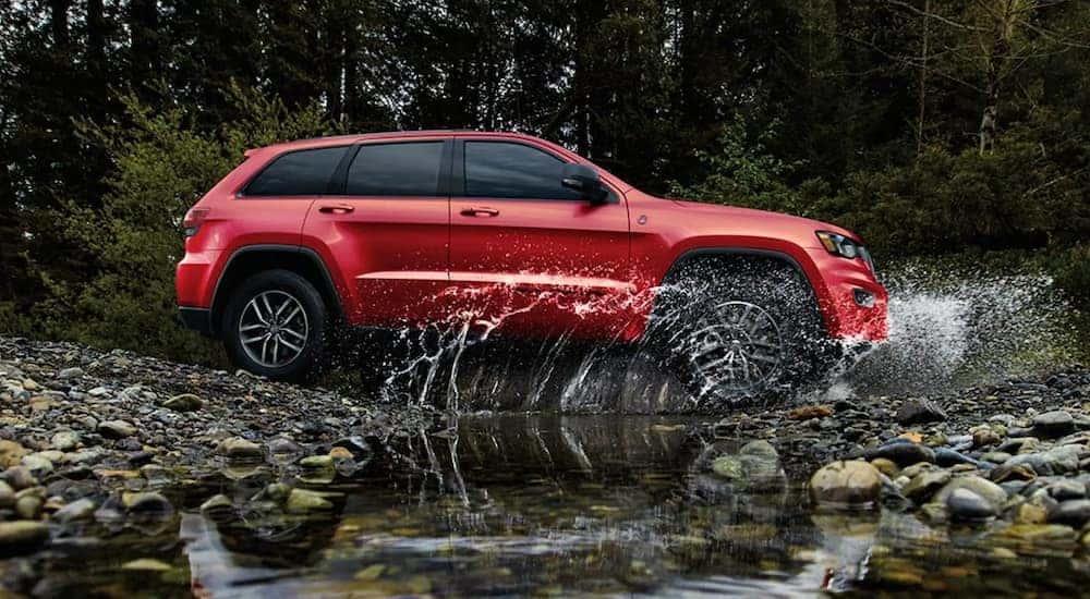 A red 2021 Jeep Grand Cherokee Trailhawk is driving through a puddle.