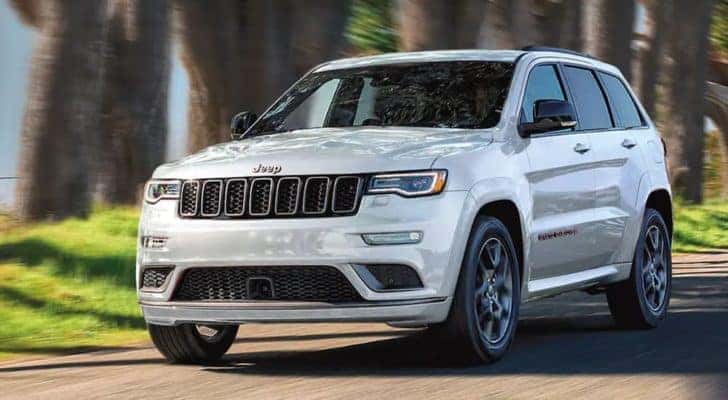 A white 2021 Jeep Grand Cherokee is driving on a tree-lined road.