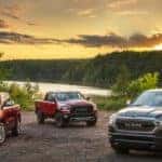 Two red and a black 2021 Ram 1500 are parked in front of a lake a sunset.