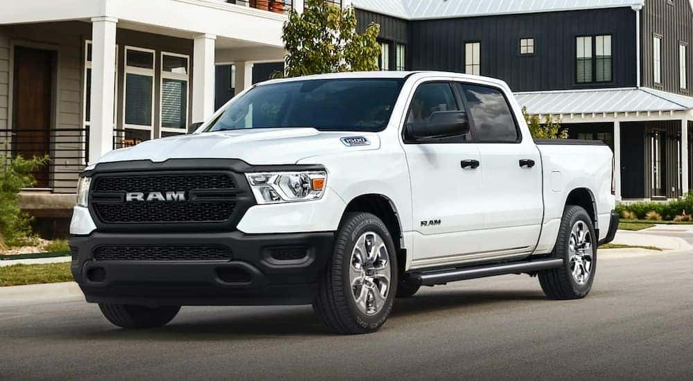 A white 2021 Ram 1500 is on a neighborhood road in front of new houses.
