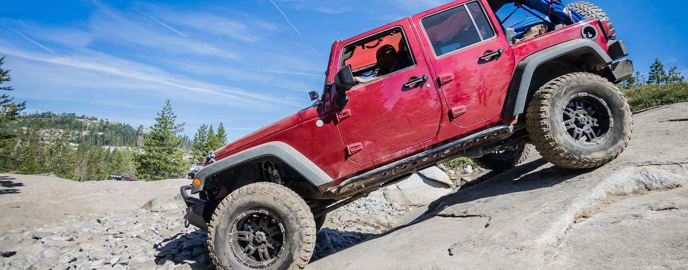 A red used 2019 Jeep Wrangler Unlimited is shown from the side rock crawling on Rubicon Trail in California.