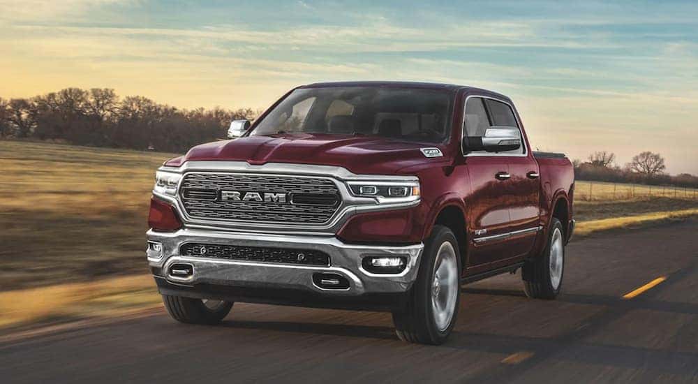 A burgundy 2020 Ram 1500 is driving on a rural road with a blue and yellow sky.