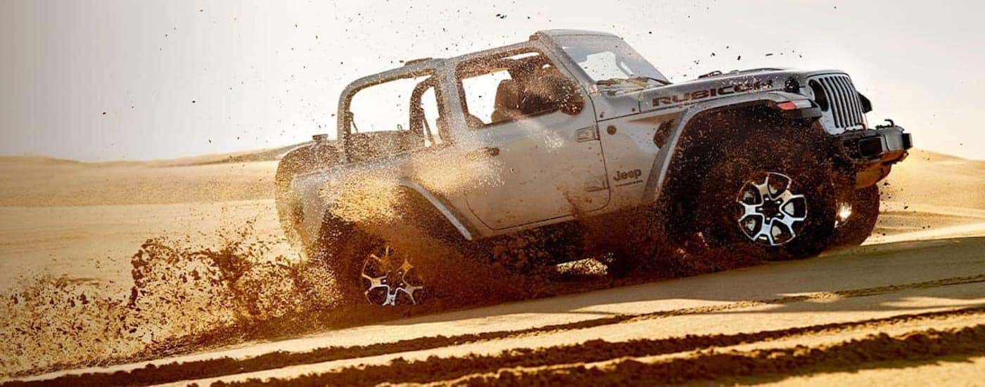 A silver 2020 Jeep Wrangler Rubicon is off-roading on beach sand after leaving a California used Jeep dealer.