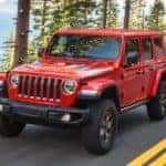 A red 2021 Jeep Wrangler is driving down a two lane road next to the ocean after leaving Jeep dealers in southern California.