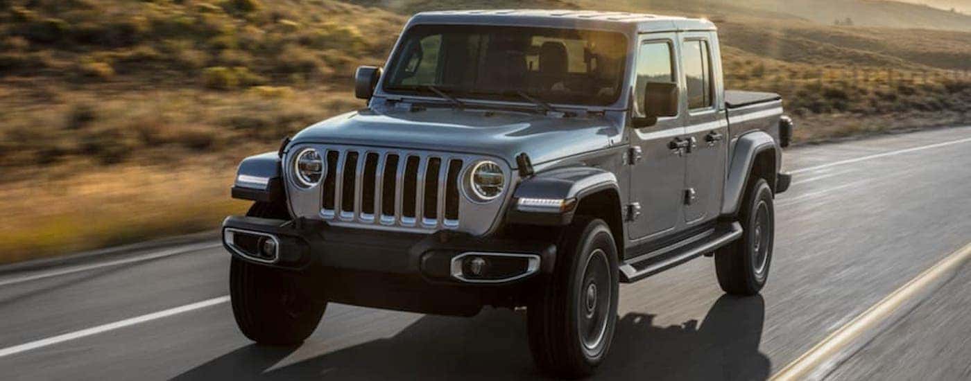 A silver 2020 Jeep Gladiator is driving on a rural road at sunset.