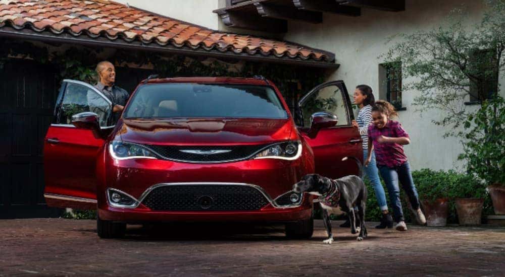 A red 2018 used Chrysler Pacifica is parked in a driveway as a family enters the vehicle.
