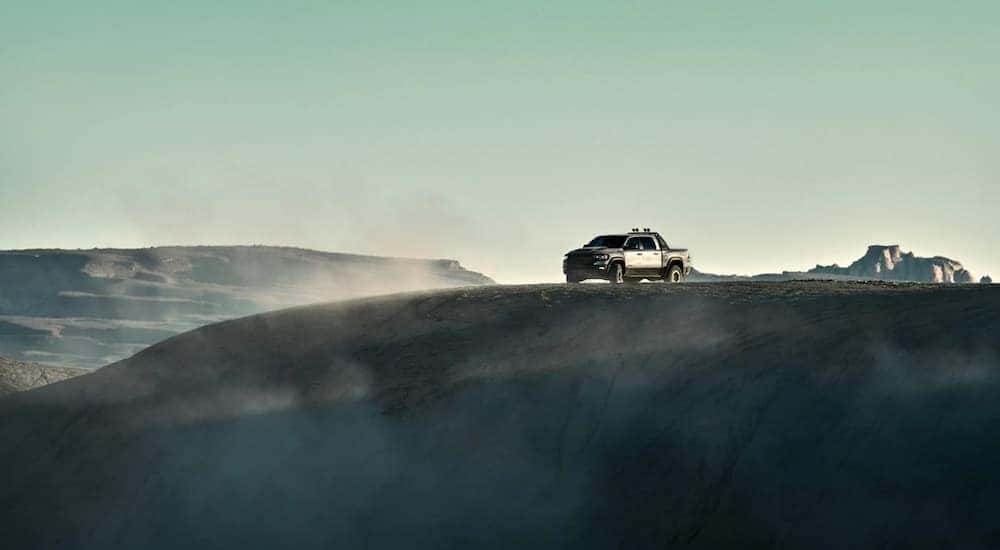 A silver 2021 Ram TRX is parked on a sandy hill in the desert.