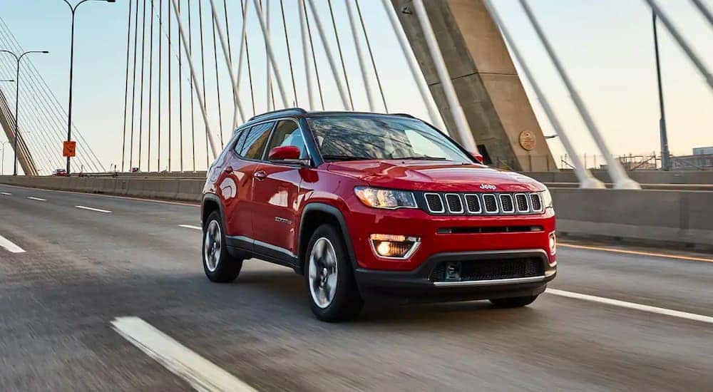A red 2020 Jeep Compass is shown driving over a bridge after leaving a used car lot.