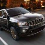 One of the most popular used cars in Costa Mesa, a black 2015 Jeep Compass, is shown driving in a city.