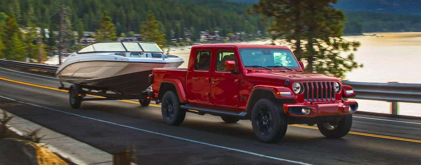 A red 2020 Jeep Gladiator is shown towing a boat past a lake.