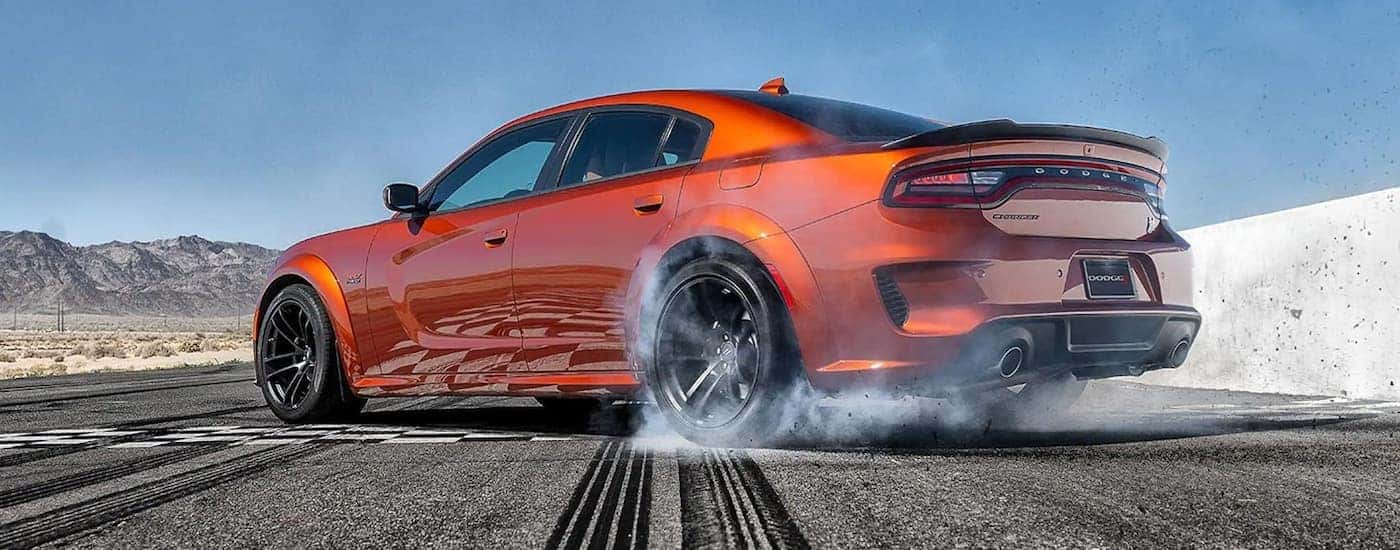 An orange 2021 Dodge Charger Scat Pack is shown from the side making tire smoke on at the race track.