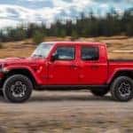 A red 2020 Jeep Gladiator is shown driving down a dirt road after leaving a used truck dealership.