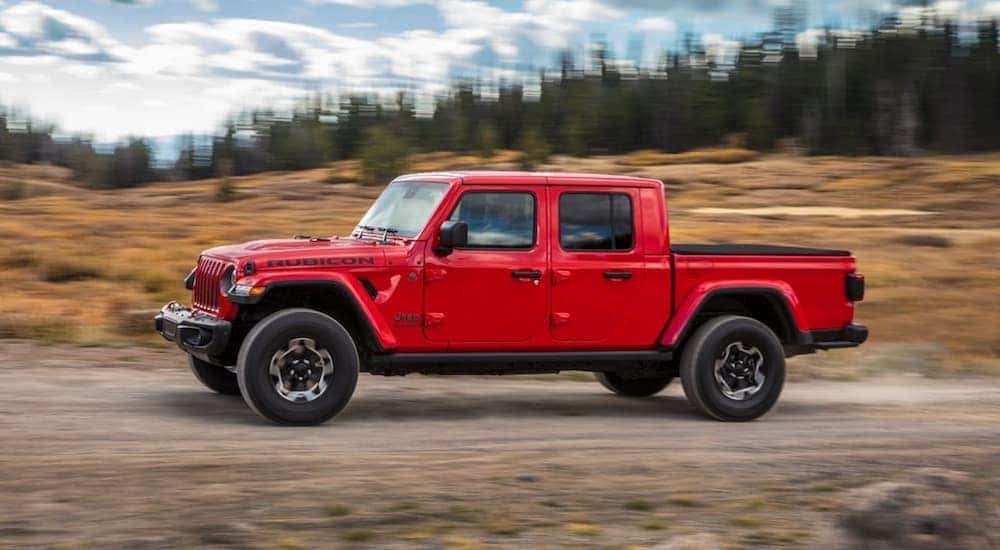 A red 2020 Jeep Gladiator is shown driving on a dirt road after after searching for used cars for sale.