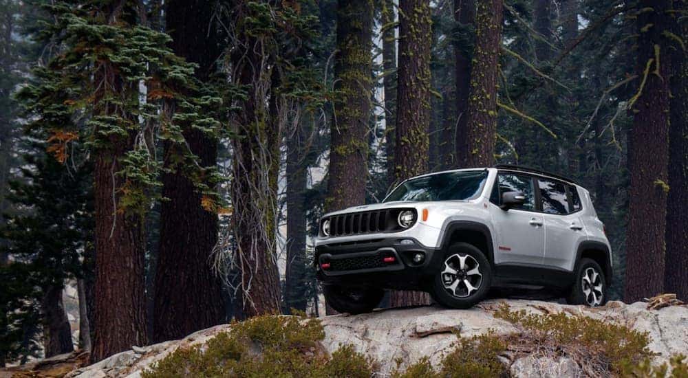 A white 2020 Jeep Renegade Trailhawk is shown parked on a large rock cliff in the woods.