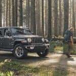 A grey 2020 Jeep Wrangler Unlimited is shown parked on a dirt road in the forest next to two hikers.