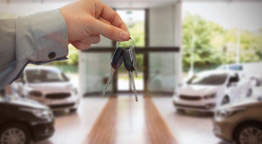 A man is holding out a set of keys inside a car dealership.
