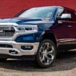 A blue 2021 Ram 1500 is shown parked in front of a red brick road.