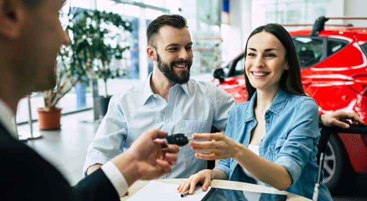 A couple is shown getting their new keys at a used car lot.