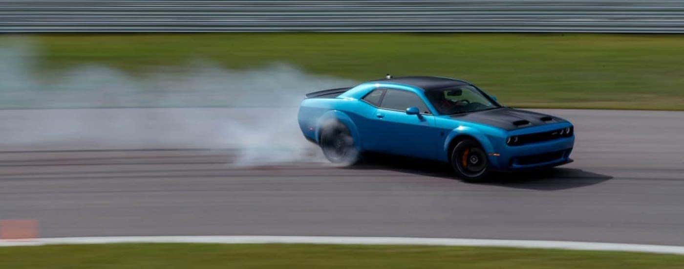 A blue 2020 Dodge Challenger is doing a burn out on a racetrack.