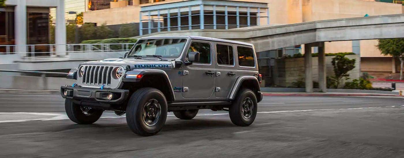 A grey 2021 Jeep Wrangler 4xe is shown driving through a city after leaving an electric car dealer.