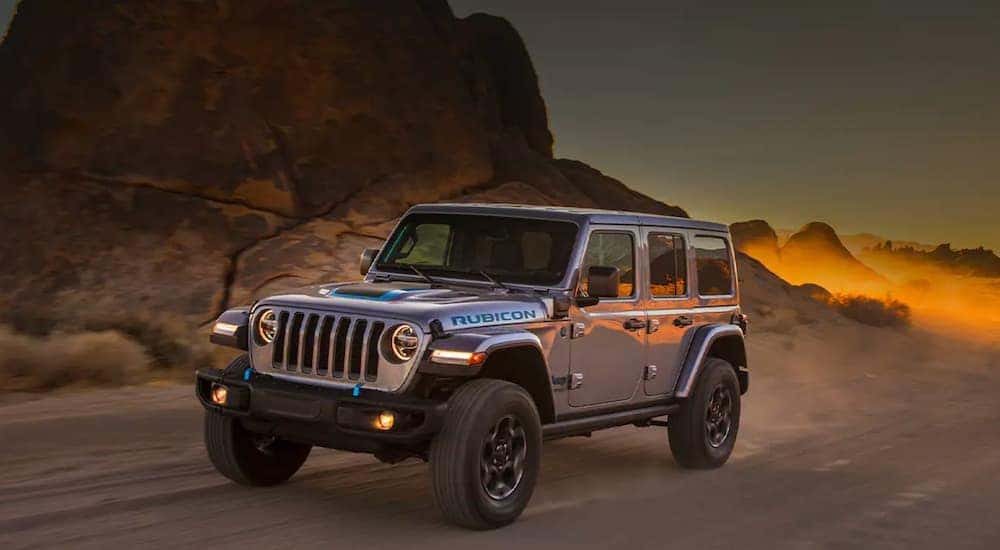 A silver 2021 Jeep Wrangler 4xe is shown from the side driving on an open road in the desert.