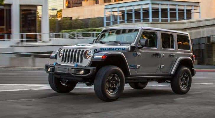 A grey 2021 Jeep Wrangler 4xe is shown driving in a city after leaving an electric SUV dealer.