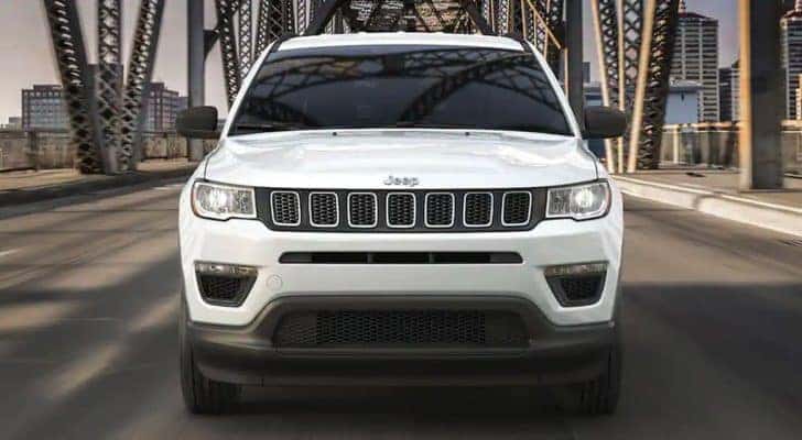 A white 2020 Jeep Compass is shown from the front driving over a bridge.