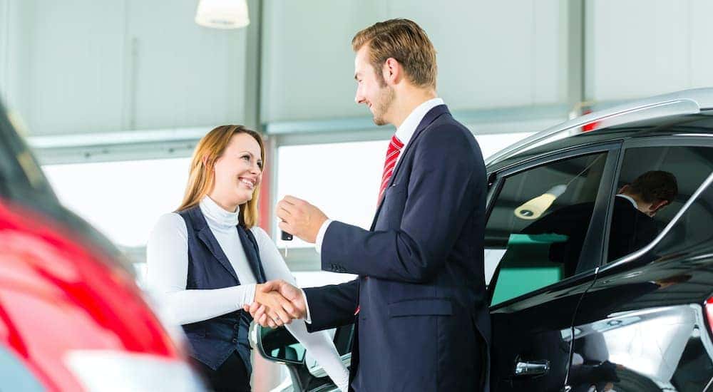 A salesman is shaking hands with a customer at a used car dealer.