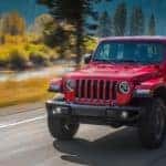 A red 2021 Jeep Gladiator is shown driving past a river.