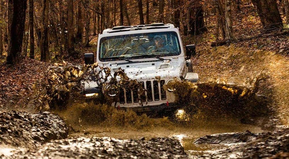 A silver 2020 Jeep Wrangler Rubicon is shown driving through a mud puddle.