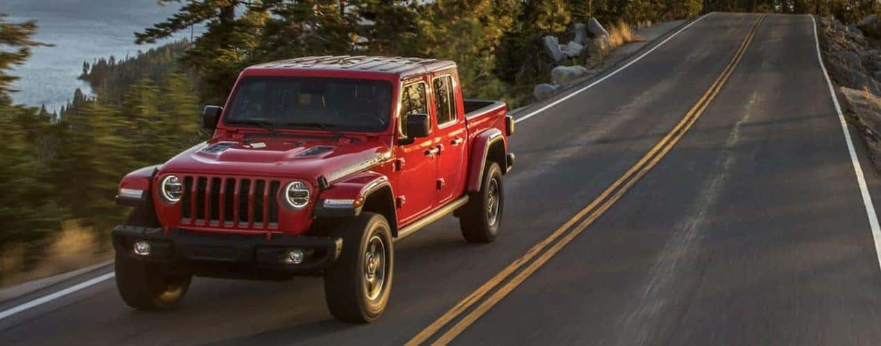 A red 2021 Jeep Gladiator is shown from the front driving on an open road past a lake.