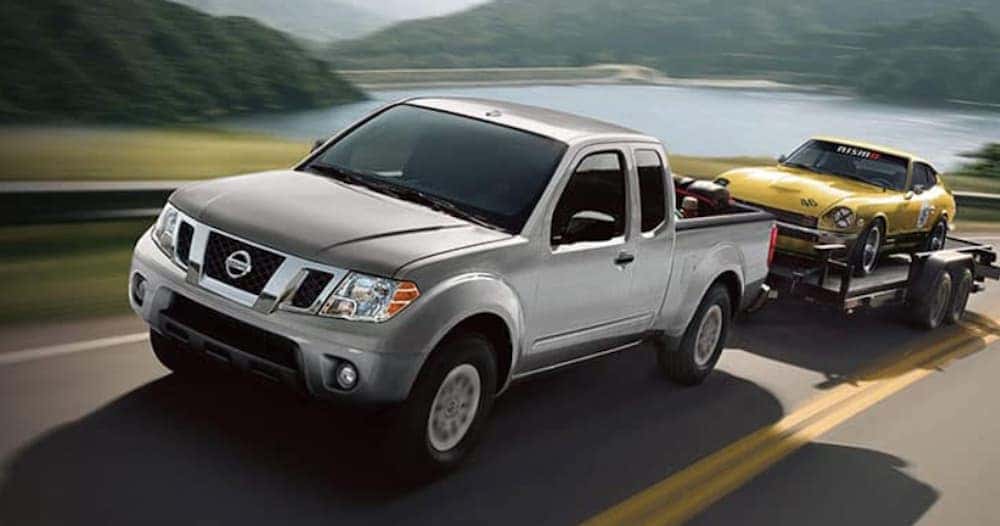 A silver 2018 Nissan Frontier is shown towing a yellow car on a trailer.