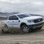 A white 2019 Ford Ranger is shown driving on a sandy beach by the ocean.