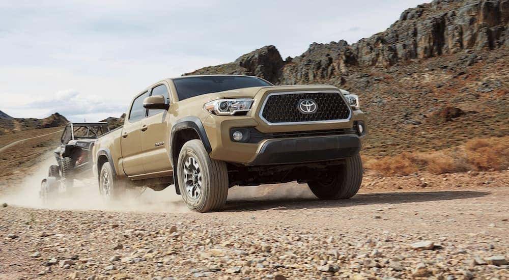 A tan 2019 Toyota Tacoma is shown towing a UTV in the desert after leaving an LA used truck dealership.