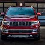 A red 2022 Jeep Wagoneer is shown from the front parked outside of a modern home.