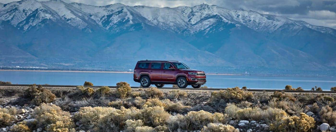 A red 2022 Wagoneer is shown from the side driving on a dirt road next to a lake.