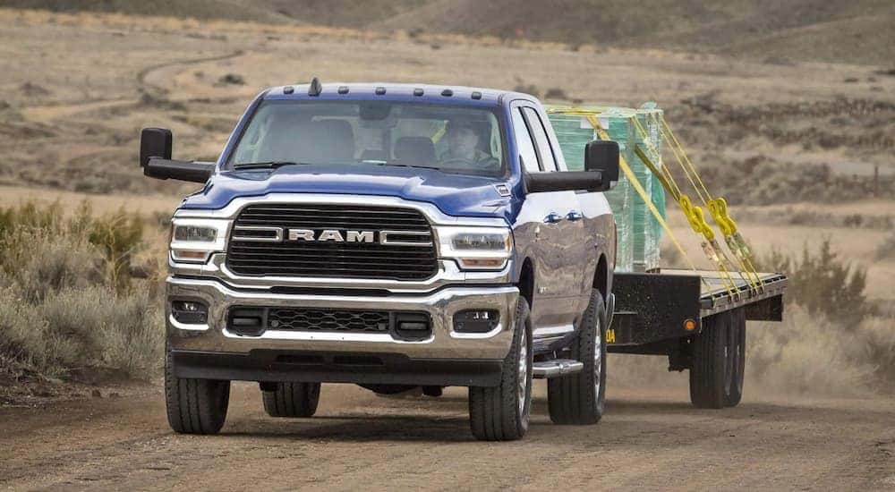 A blue 2021 Ram 2500 Big Horn is shown towing a trailer with supplies on a dirt road.