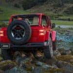 A red 2021 Jeep Wrangler Rubicon is shown from the rear off-roading on a rocky area.
