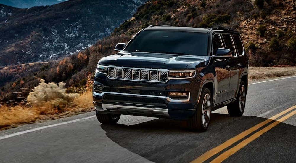 A black 2022 Grand Wagoneer is shown driving on a highway through the mountains.