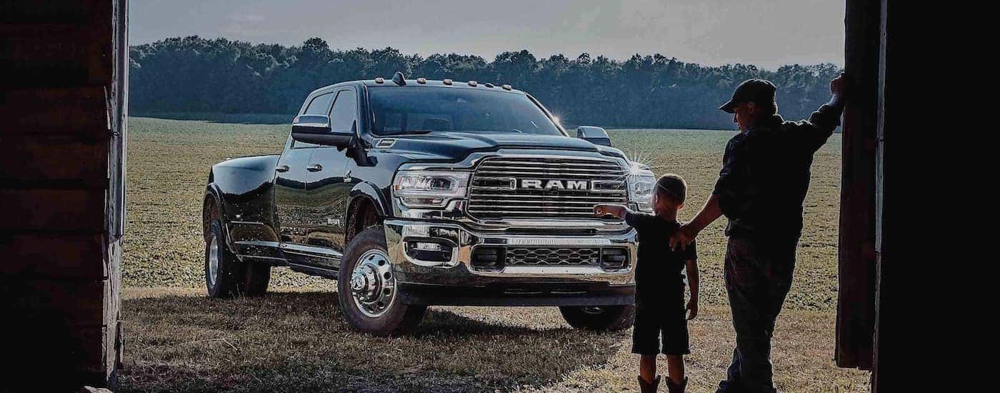 A father and son are looking at a 2022 Ram 3500 that is parked outside of a barn.