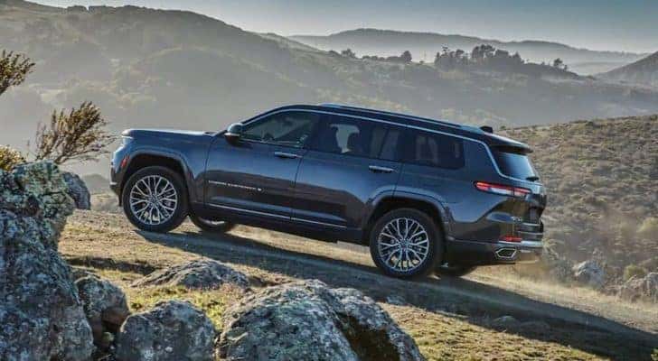A blue 2021 Jeep Grand Cherokee L is shown from the side off-roading in the mountains.