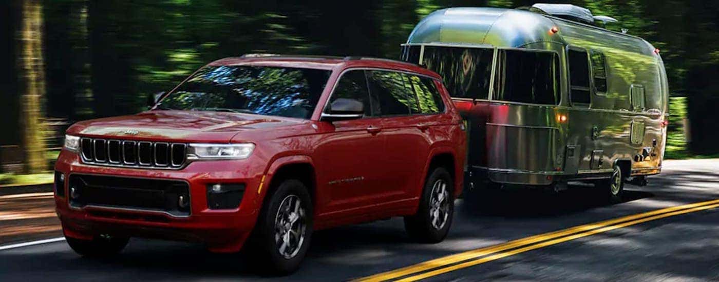 A red 2021 Jeep Grand Cherokee L is shown towing a trailer.