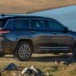 A grey 2021 used Jeep Grand Cherokee is shown driving on grass near a body of water.