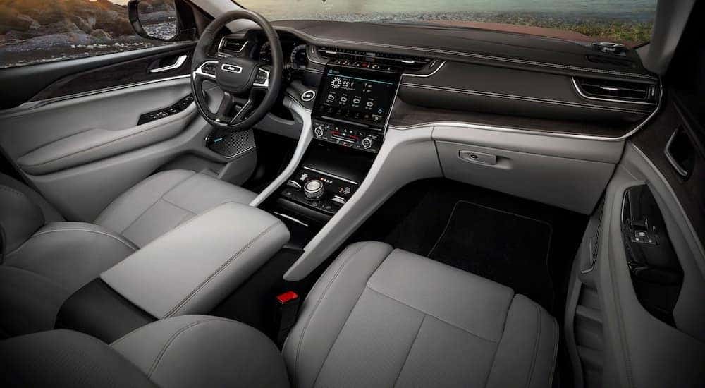The black and grey interior of a 2022 Jeep Grand Cherokee L shows the steering wheel and infotainment screen.