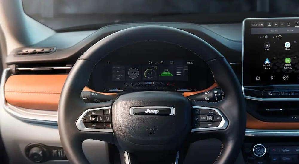 A close up of the black and brown interior of a 2022 Jeep Compass shows the steering wheel and infotainment screen.
