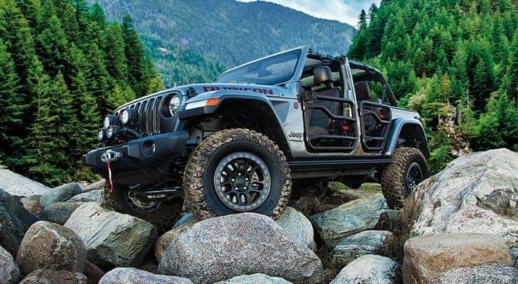 A silver 2021 Jeep Wrangler Rubicon Unlimited is shown off-roading on large rocks.