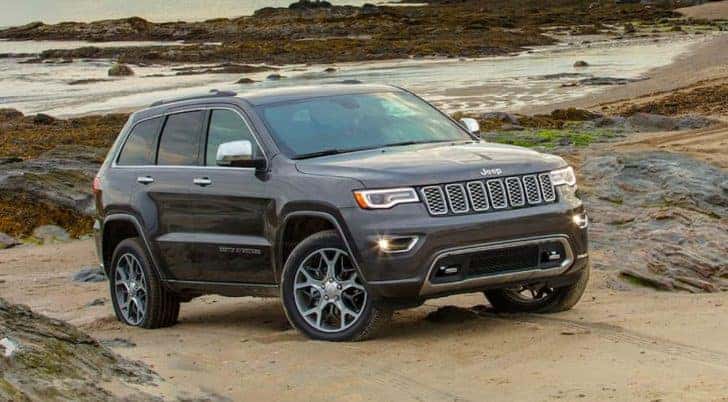 A grey 2020 Jeep Grand Cherokee is shown parked on a beach after leaving a certified pre-owned Jeep dealership.